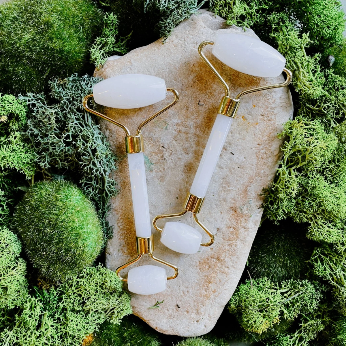 Two facial roller devices on a stone with green foliage in the background