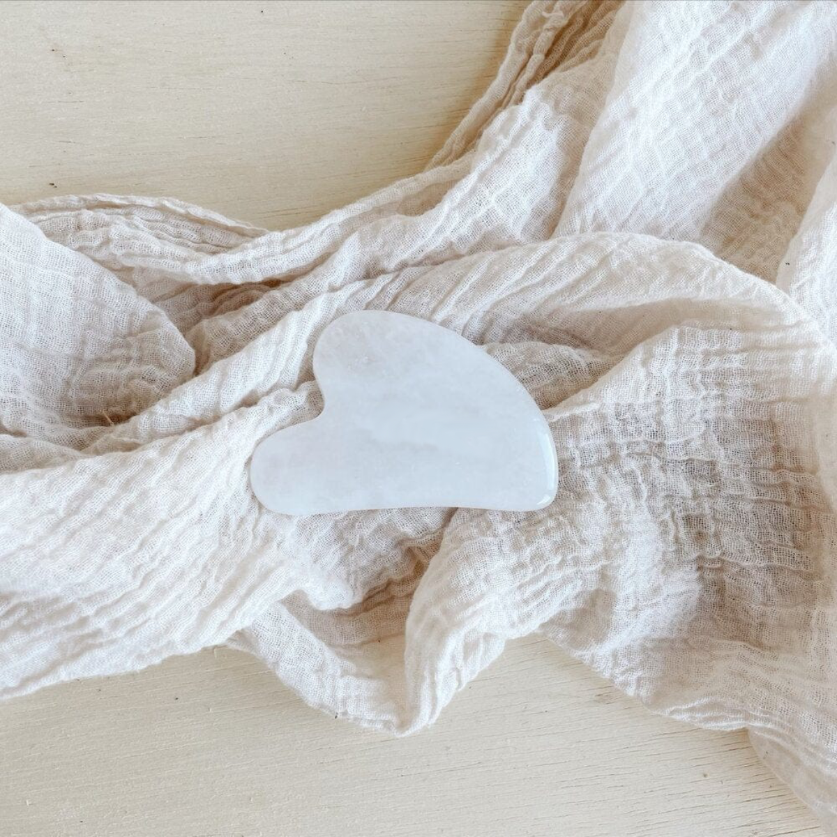 White gua sha tool on a textured white fabric background